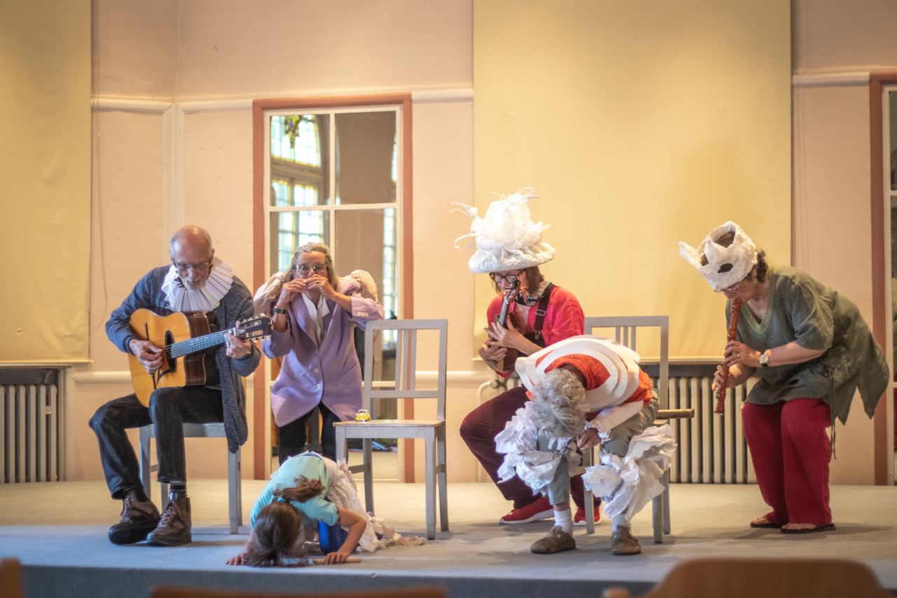 Musiker:innen mit Gitarre, Muntamonika und Blockflöte sitzen auf Stühlen. Sie sind verkleidet.