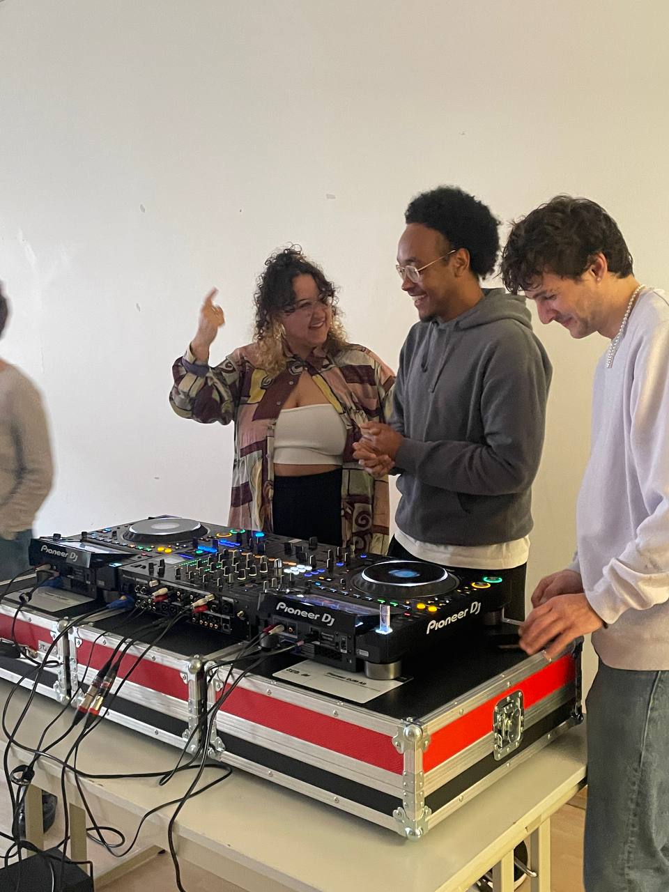 Drei junge Erwachsene stehen vor einem Dj Pult.