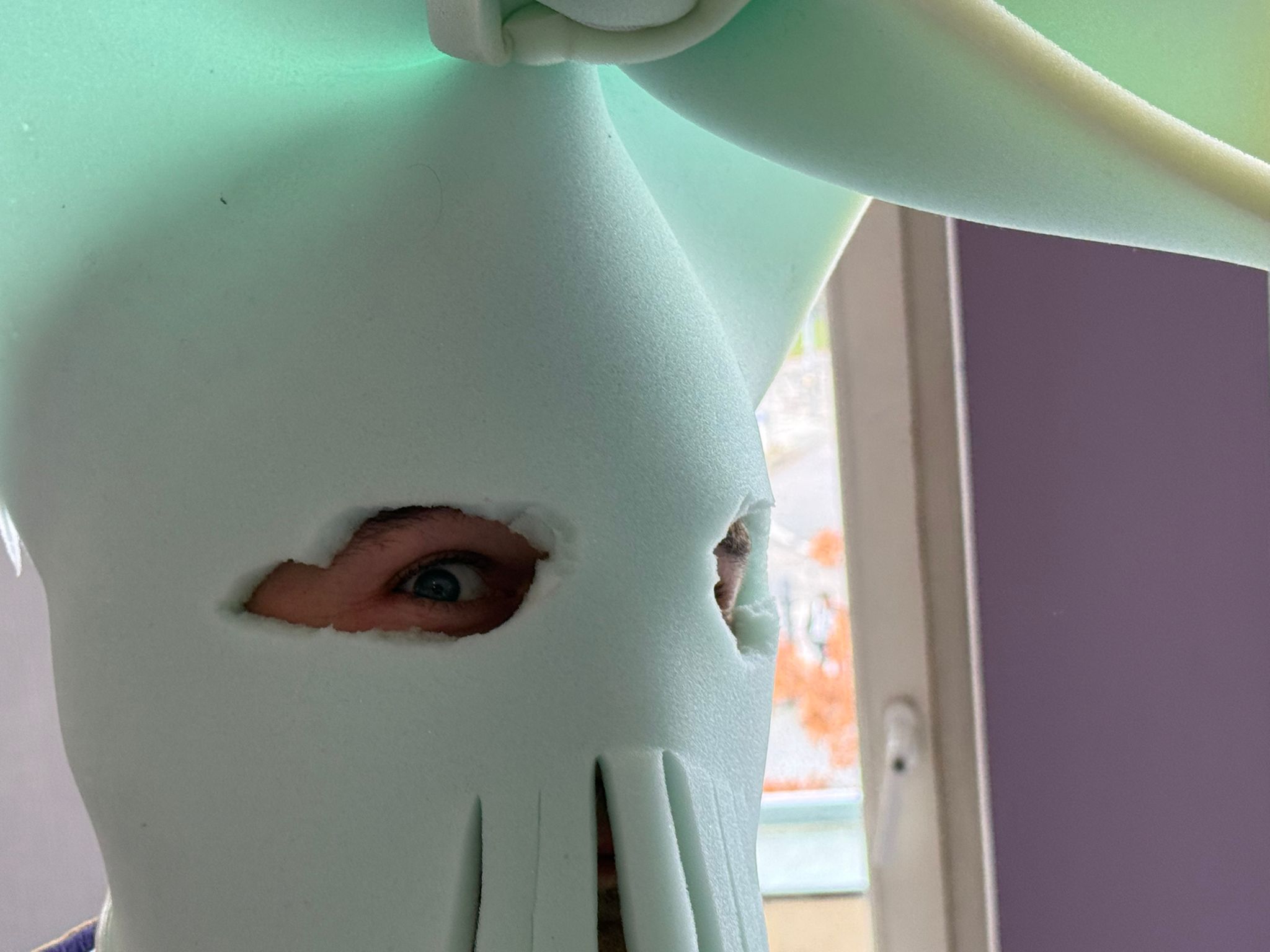 Ein Kind schaut in die Kamera. Es hat eine Maske auf die das gesamte Gesicht bedeckt und die Augen ausspart. Die Augen sind weit aufgerissen.