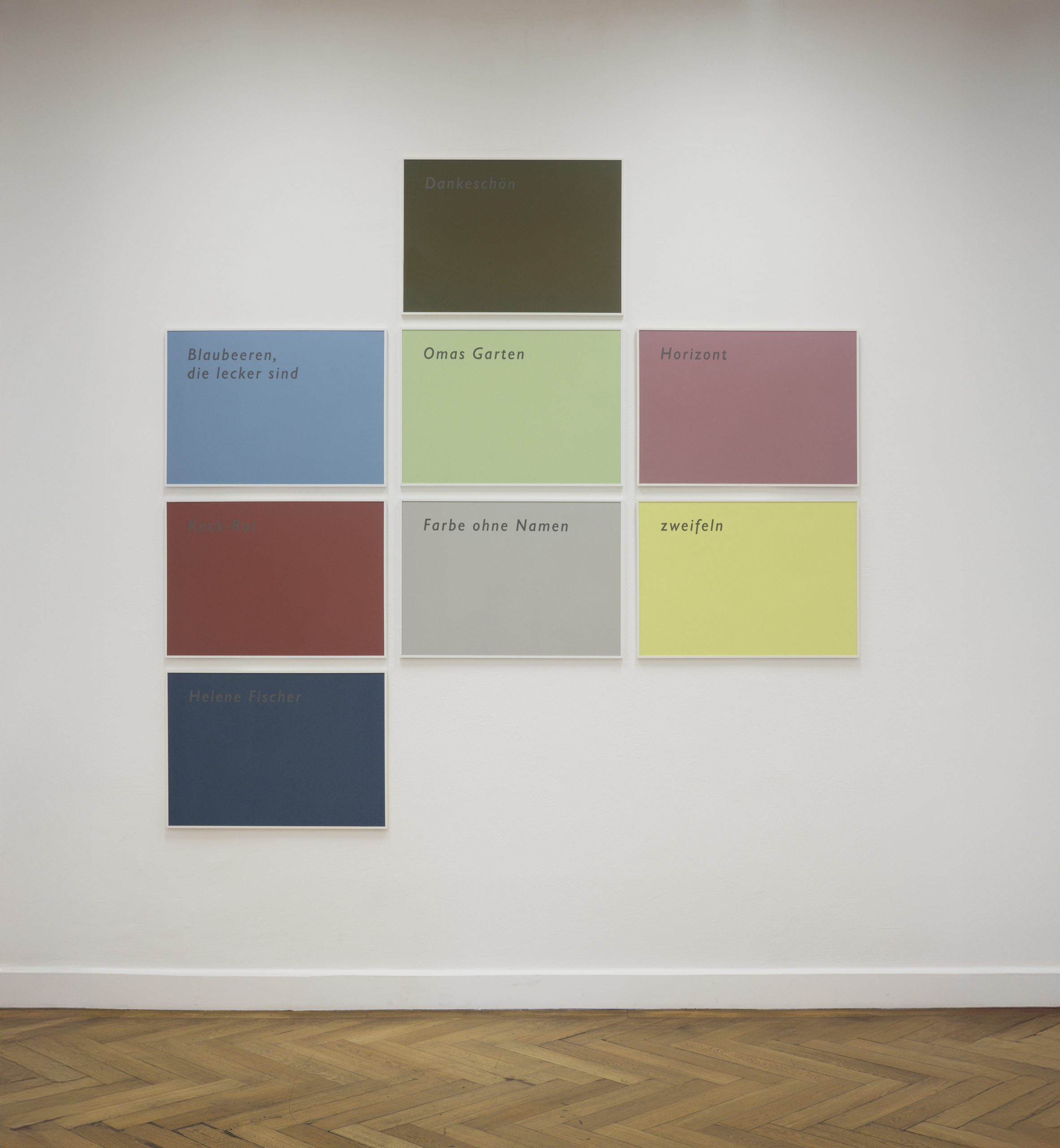 An einer weißen Wand hängen 8 Tafeln in unterschiedlichen Farben.